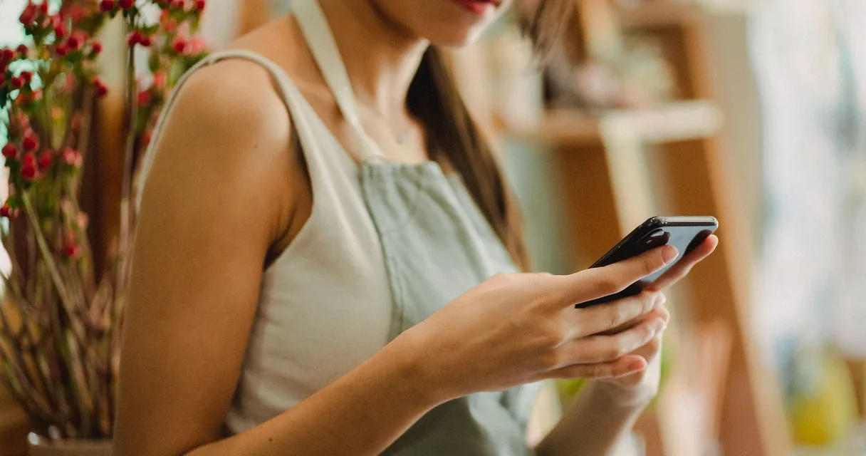 Dona de uma loja segurando um celular enquanto consulta uma resposta