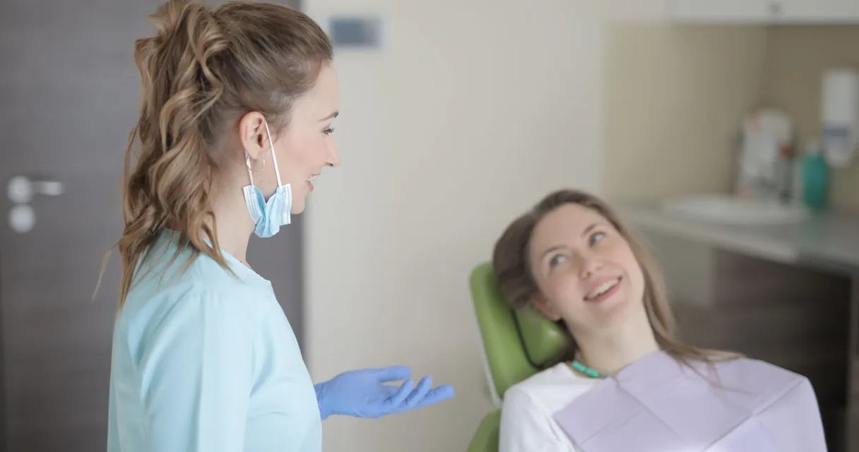 Dentista conversando com uma paciente na cadeira de um consultório odontológico
