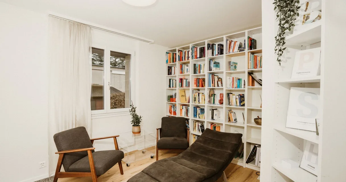 Consultório de psicologia com poltronas, estante de livros e luz natural